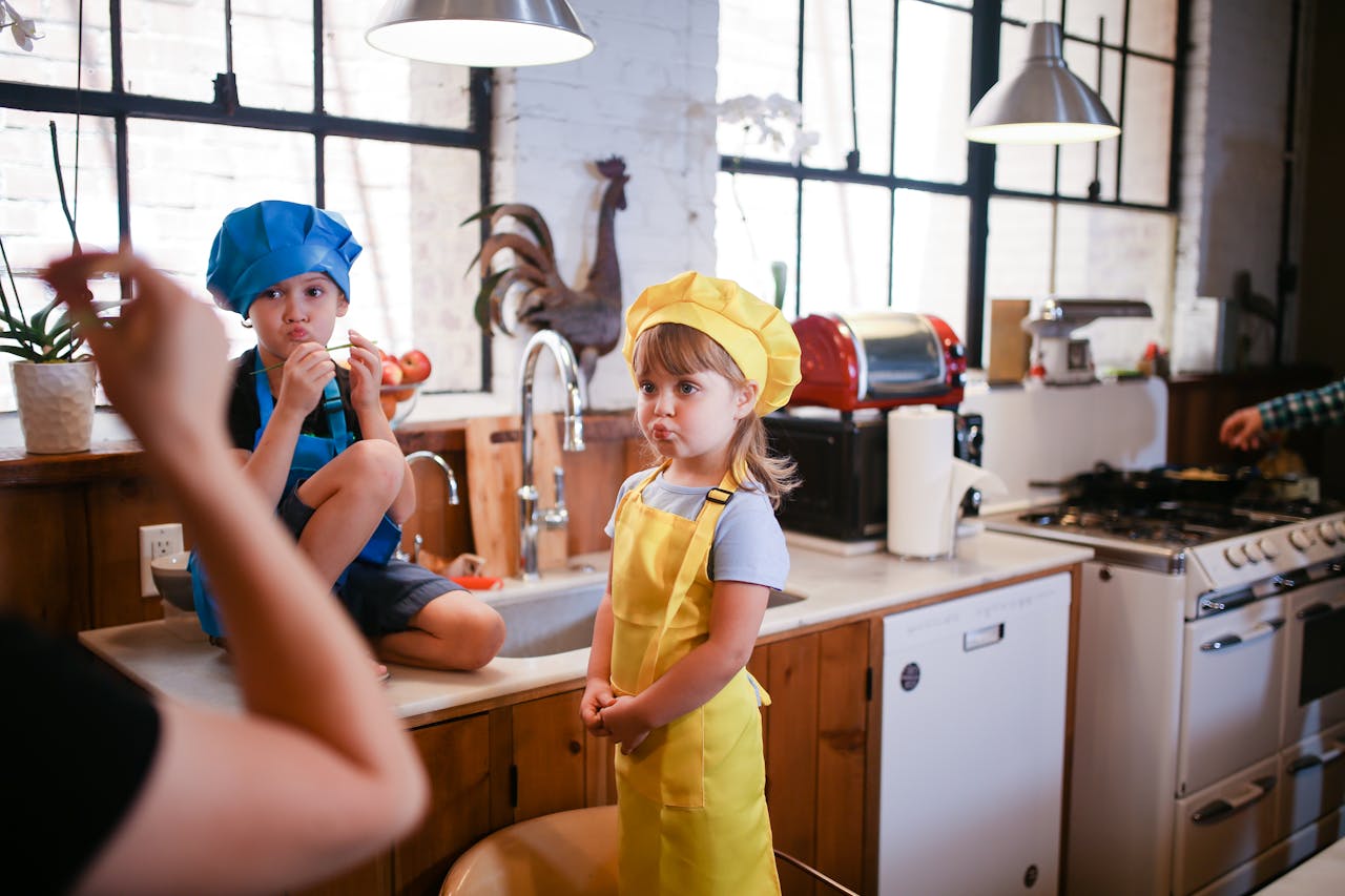 Home Two kids in colorful chef hats enjoy a playful cooking session in a cozy kitchen setting.